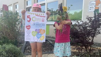 Zwei Kinder aus dem Inklusiven Campus zeigen das Festplakat und halten einen Blumenstrauß als Willkommensgruß. | Foto: Isabel Lubojanski / Caritas